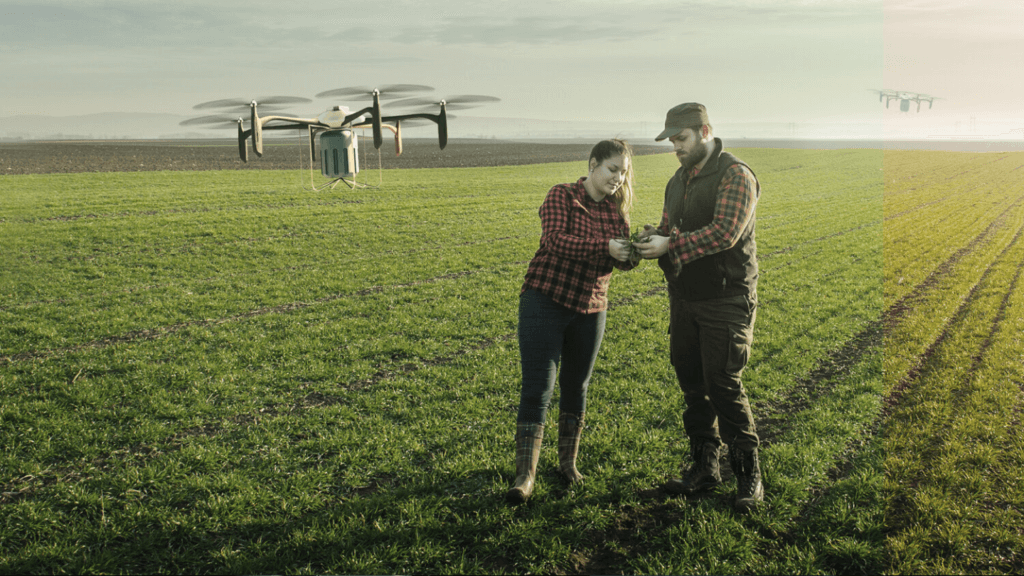 Two people stand in a field controlling a drone which flies nearby